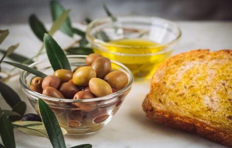 Closeup shot of slices of bread with extra virgin oil near glass bowls filled with oil and olives
